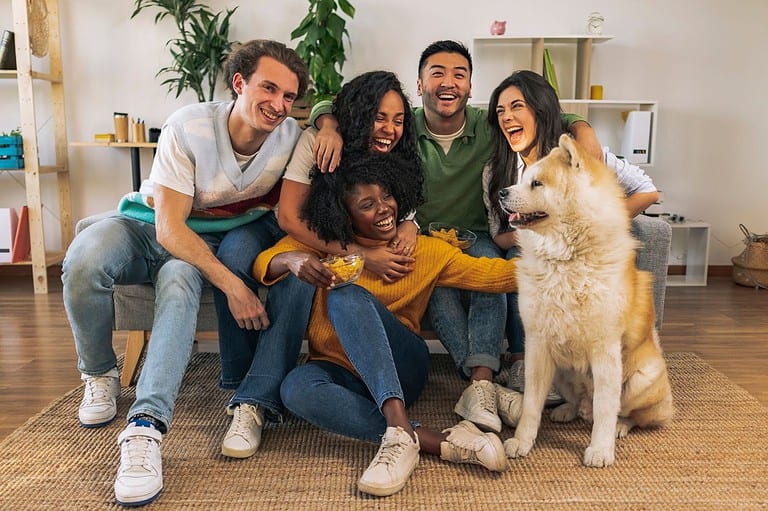 A diverse group of friends laughing and smiling with their dog at Jokes About Dogs - Clean Jokes You Can Tell Your Family