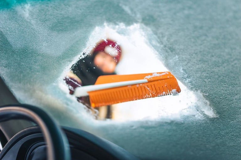 A person scrapes the windshield of their car on a cold winter day.