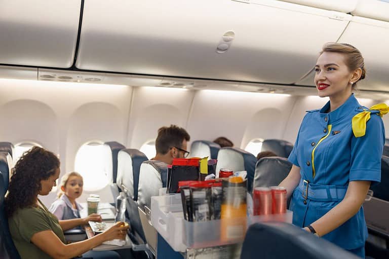 Flight attendant serving travelers in an airplane. You won't believe this pro tip for travelers! Stay healthy and hydrated on your next flight with this simple beverage choice! What is it?