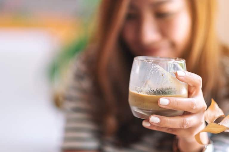 Asian woman enjoys drinking an iced coffee. Experience the rich flavors of Vietnam at Minneapolis' first Vietnamese coffee shop, Càphin! Discover the unique taste of Robusta beans!