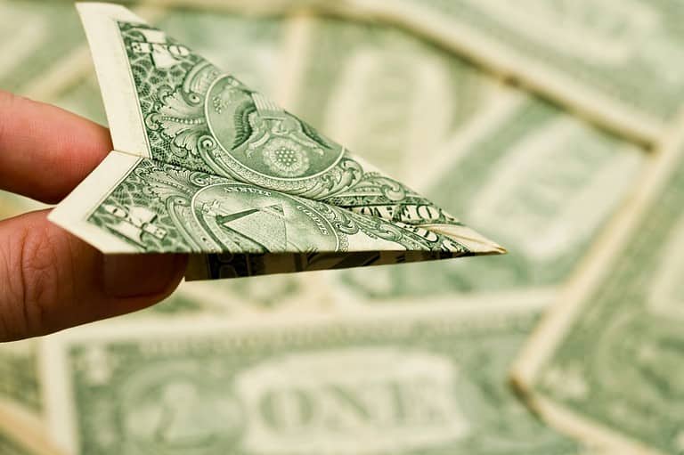 A man holds a paper airplane made of a dollar bill. Are you always on the lookout for cheap flights? Want to fly for less? Find out the best time to book your flight and save big!