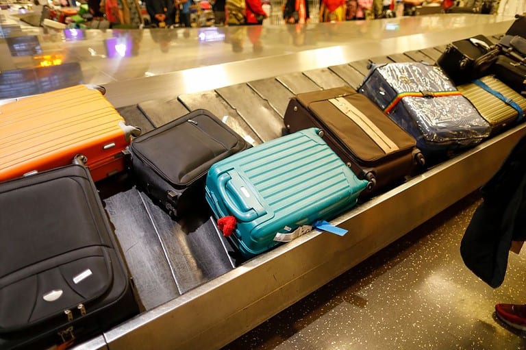 Suitcases at baggage claim. Want to beat the baggage claim blues? Check out these 6 tips to get your luggage first! These secrets might just give you a head start!