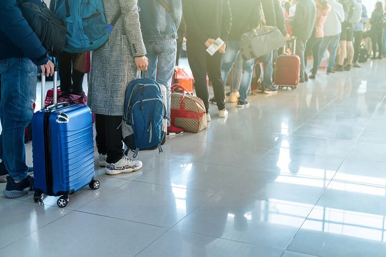 Long line of weary travelers holding luggage at the airport. Skip the long customs lines with Global Entry and breeze through airport security! This helpful guide will let you know all the details.