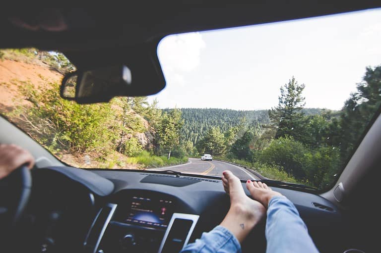 A couple on a summer road trip. The woman has her feet on the dashboard and the northern Minnesota scenery is seen through the windshield. Ready for a road trip? Join us on a 150-mile scenic adventure from Duluth to Grand Marais along Highway 61!