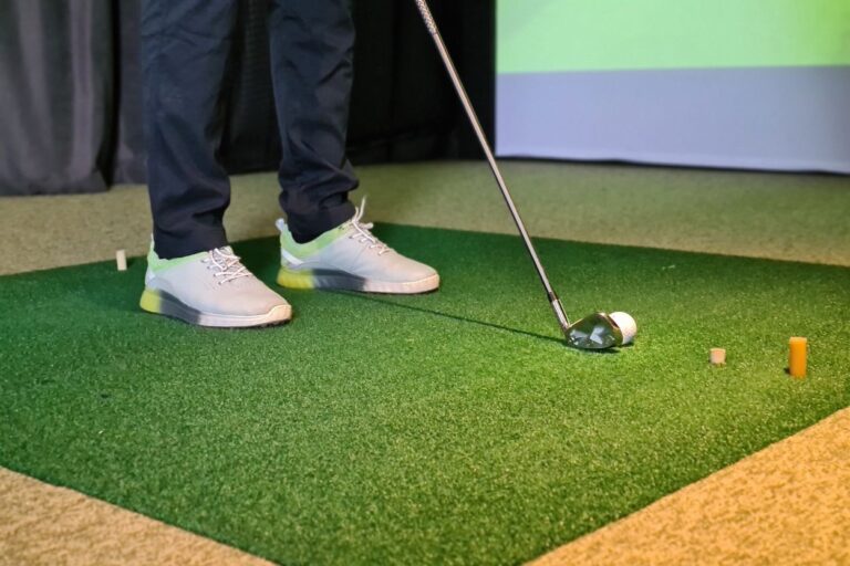 Indoor golfer wearing golf shoes and holding a golf club gets ready to practice at Winona Minnesota's indoor golf center.