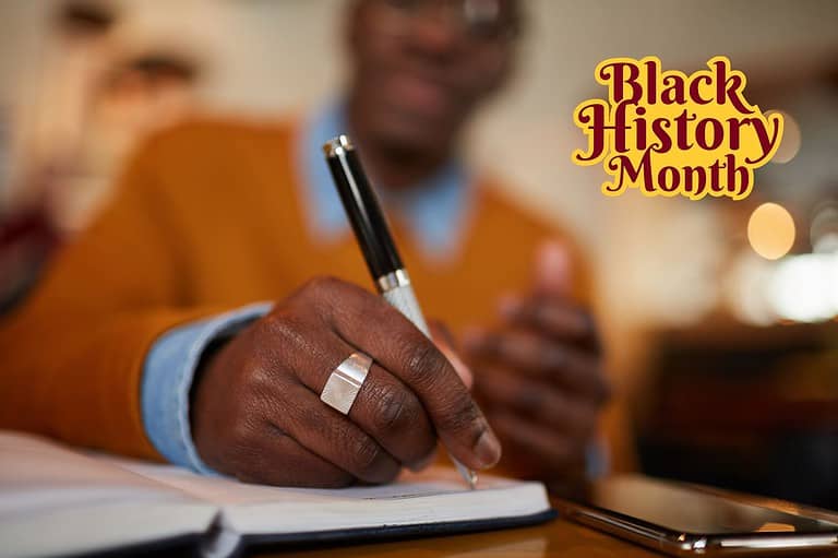 African American man writing poems in a notebook with a pen. Close-up of his hand. Discover J. Otis Powell, Minnesota's legendary spoken word poet, who bridged cultures and communities with his powerful words.