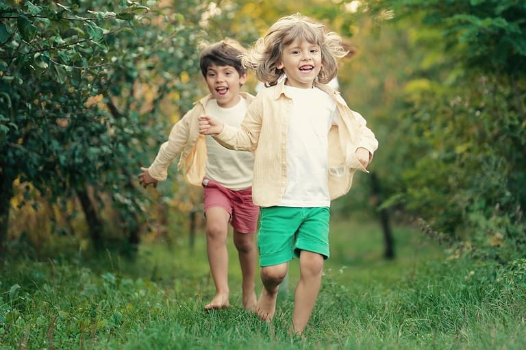 Kids running through lush green grass with rich forest of trees at Minnesota's nature-themed playground