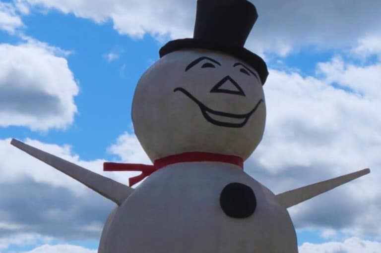 Blue skies behind the World's Largest Stucco Snowman in North St Paul, MN. He is smiling and wearing a black top hat.