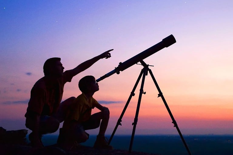 Father and son with telescope pointing at the sky. It is sunset with purples, oranges and pinks. UFO Seen Over Bismarck, North Dakota's Liberty Memorial Bridge