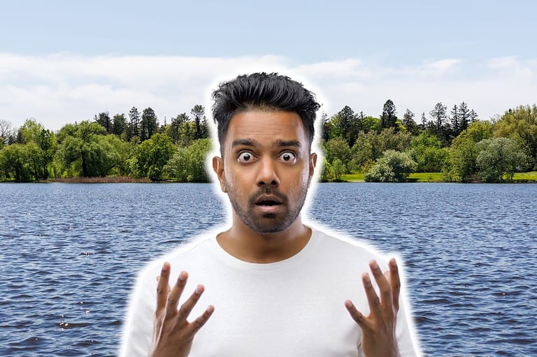 Shocked man in front of serene lake in Iowa. Uncover the hidden history beneath Iowa's Lake Red Rock and explore the remnants of six submerged towns on your next outdoor adventure!