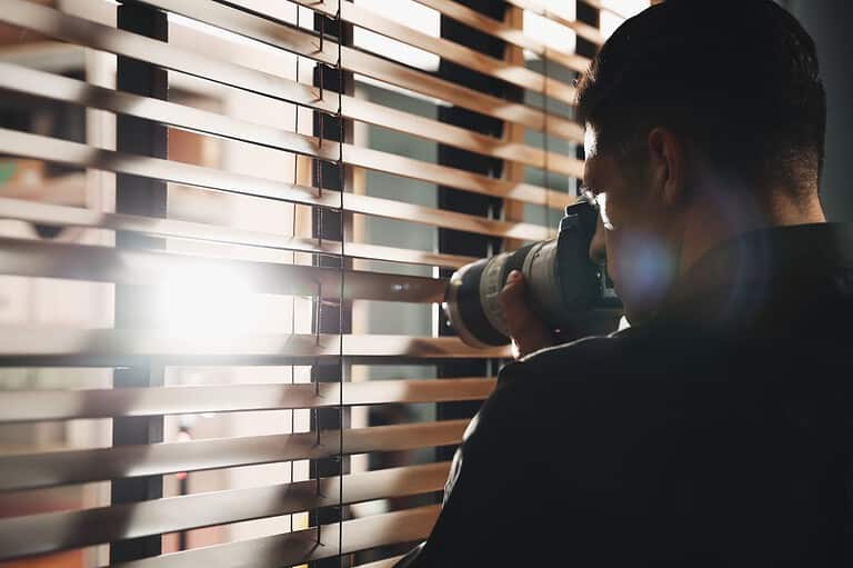 Creeping man spying through a window. Say goodbye to indoor security cameras on your next Airbnb stay! The company is FINALLY banning them worldwide for better guest privacy.