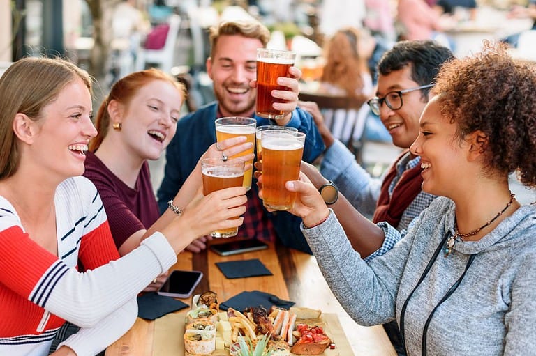 Happy people drinking beer at a table. They are smiling and clinking glasses. Experience a sensory explosion at the Between the Bluffs Beer, Wine and Cheese Festival! Sip, savor, and swing to the rhythm of celebration!