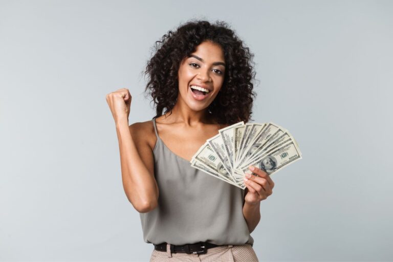 Woman happy to be holding a stack of cash money. ATTENTION REMOTE WORKERS! These US cities are offering INSANE incentives for you to move there, and we've got the scoop!