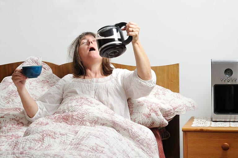 Funny photo of tired woman in bed drinking coffee straight from the pot! Need a little pick-me-up? Check out our latest post for some hilarious coffee jokes that will brew a smile on your face!