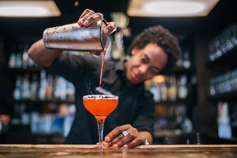 Bartender pours drink in Minneapolis. While traveling, these are the drinks you should steer clear of when bellying up to the bar. Why avoid these bar drinks? Find out now!