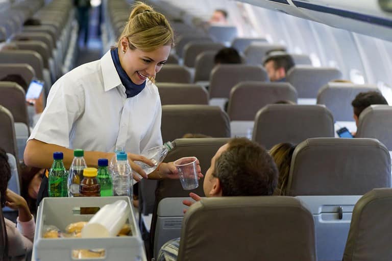Flight attendant serving drinks to man. Ready to fly smarter and score some sweet perks? These secret tips will have you living the high life at 30,000 feet—without spending a dime!