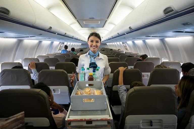 Happy flight attendant with food serving cart. Discover the unexpected joys of ginger ale on your next flight and elevate your travel experience to new heights!