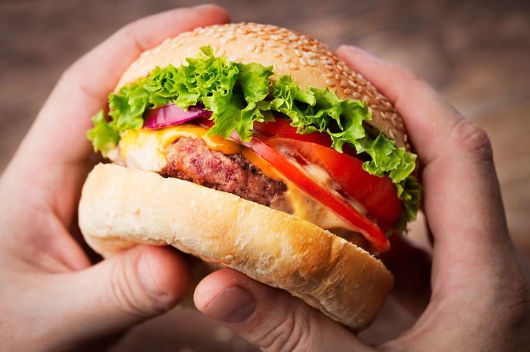 Man holding a delicious looking hamburger. You'll never guess why hamburgers are called hamburgers! The shocking truth behind America's favorite sandwich will blow your mind!