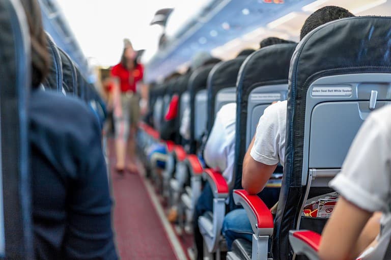 Flight attendant walking down airplane aisle. Unlock the secret to a more comfortable flight with this little-known airplane seat hack! This simple tip will change the way you fly!
