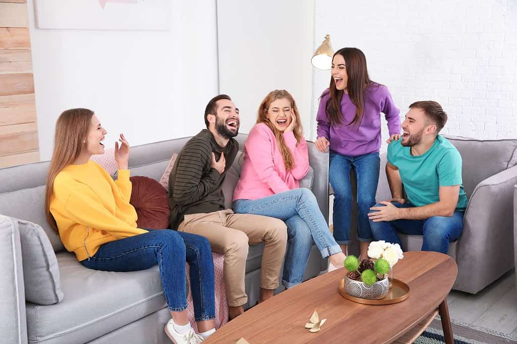 Group of friends sitting on a couch in a living room laughing at short jokes. Find the best short jokes that are clean, easy to remember, and perfect for making your family laugh.