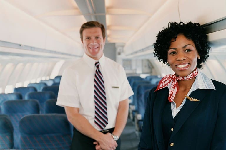 Two flight attendants ready to greet passengers on the plane. Have you ever noticed that flight attendants sit on their hands during takeoff and landing? The reason why is surprising!