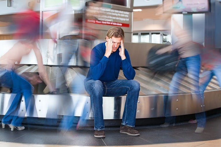 Stressed man at busy airport baggage claim. Experience the joy of stress-free travel. You'll never travel the same way again after discovering this mind-blowing iPhone trick!