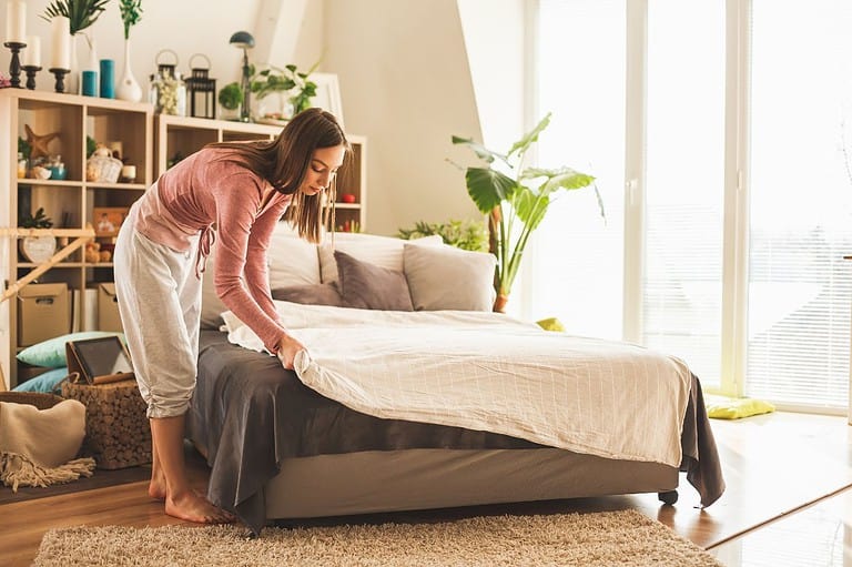 Woman making her bed. You'll never look at your sheets the same way again after reading this! Find out how often you should *really* be washing them.