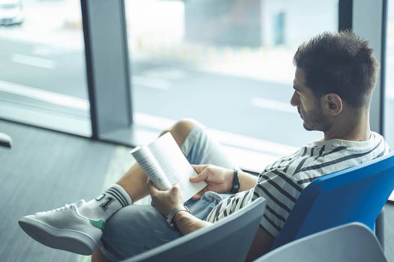 Man reading book at MSP International Airport in Minnesota. Attention all Midwestern travelers! Did you know about this amazing airport bookstore secret? It's a traveling bookworm's best friend!