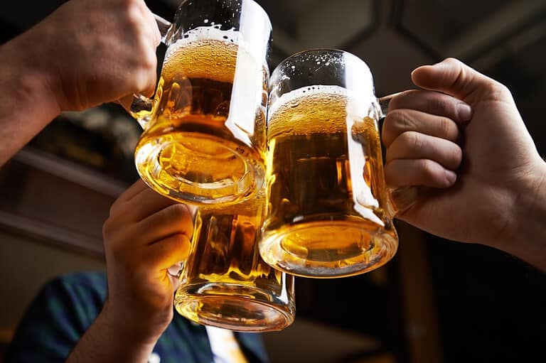 Pints of beer held up over a toast. Looking for a laugh? Check out these 66 hilarious beer jokes that are perfect for sharing with friends over a pint!
