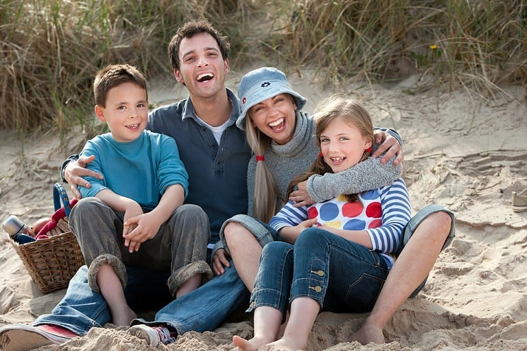 Family at beach, laughing. Make a splash with our collection of hilarious Beach Jokes, Swimming Jokes, and Pool Jokes that will have you cracking up all summer long!