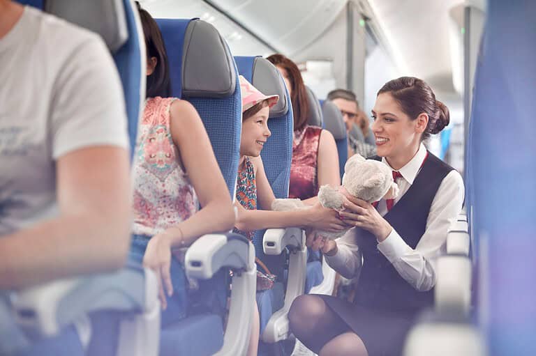 Flight attendant in crowded plane talks to kid. Want to become a flight attendant? A life of endless adventure, free travel, and unforgettable experiences awaits!