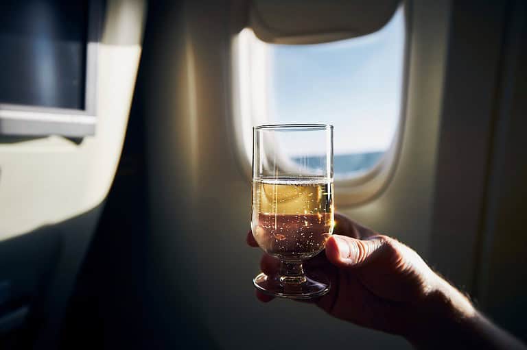 Man holding up a drink in an airplane. Straight from a flight attendant's lips: the little-known secret to getting complimentary cocktails at 30,000 feet!