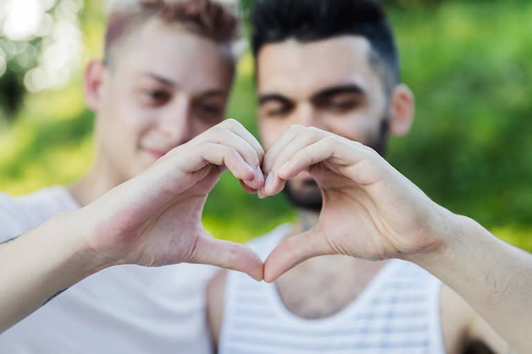 Gay couple making a heart with their hands in the park. Uncover the vibrant LGBTQ+ scene and stunning landscapes of Minnesota with this ultimate travel itinerary!