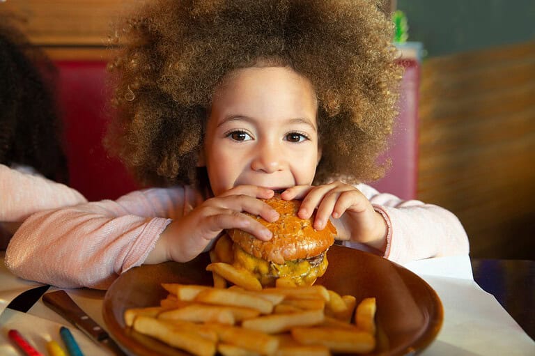 Little kid eating big burger at restaurant