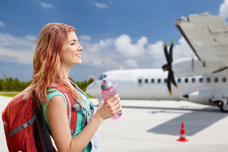 Happy woman with water bottle near an airplane