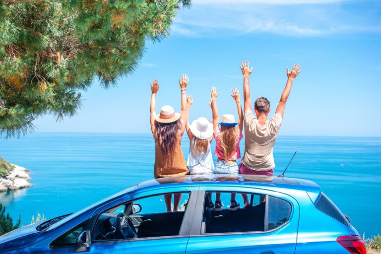 Happy family sitting on top of car at lake. Before you hit the road, make sure your car is ready for adventure with these expert answers to your top road trip questions!