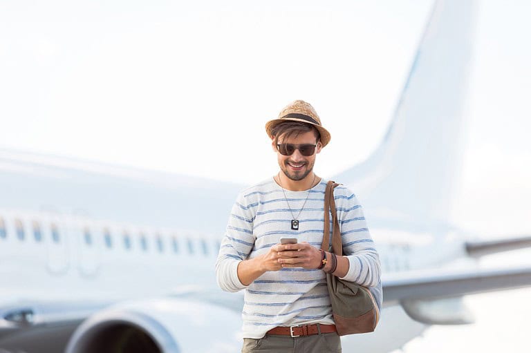Man using phone near plane. Looking for reliable wi-fi in the sky or at the airport? Find out which airlines and airports are best...and worst!