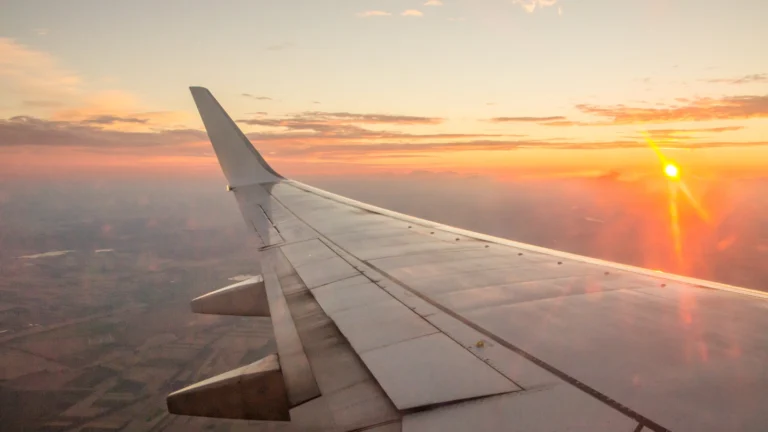 Airplane wing at sunrise. Flying early isn't just smart; it's essential! Discover why early morning flights are the ultimate travel hack for having a smoother journey.