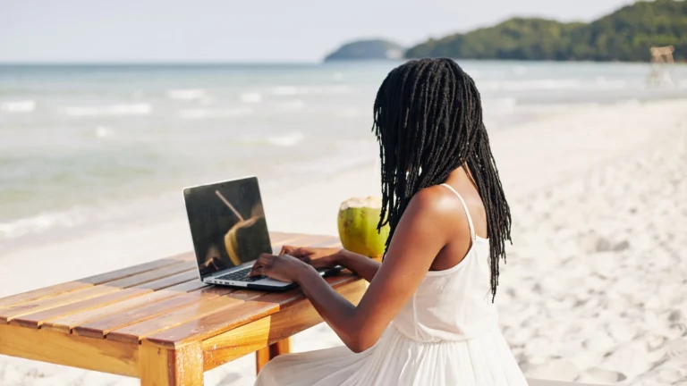Woman with laptop on tropical beach. Remote workers are turning their desks into travel hotspots by "quiet vacationing" during work hours - and sparking a nationwide debate.
