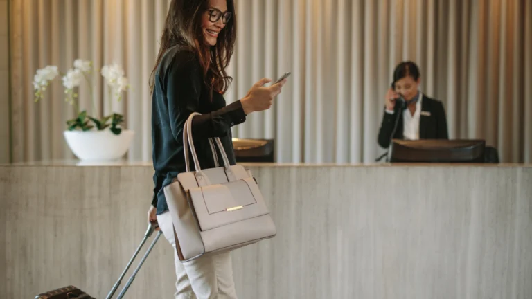 Business woman on a bleisure trip in hotel lobby looking at phone. Forget boring business trips—this explosive new travel trend is shaking up how we work and play, and it’s raking in billions!